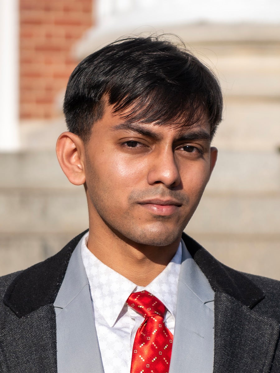 Headshot of Rustam Biswas in a suit jacket with a red tie on a sunny day
