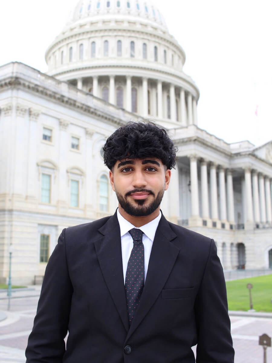 Headshot of student wearing black suit and navy tie