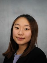 Emily Yi's headshot photo features her with in a black blazer with a gray background.