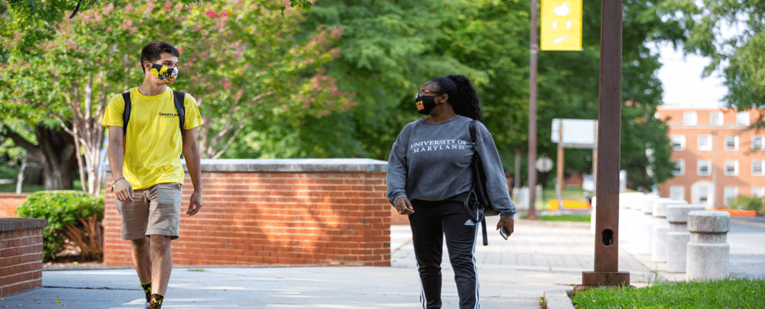 Two students walking outdoors while social distancing. 