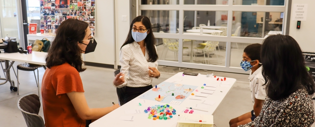 Three students sit around a table discussing their work as accelerator fellows