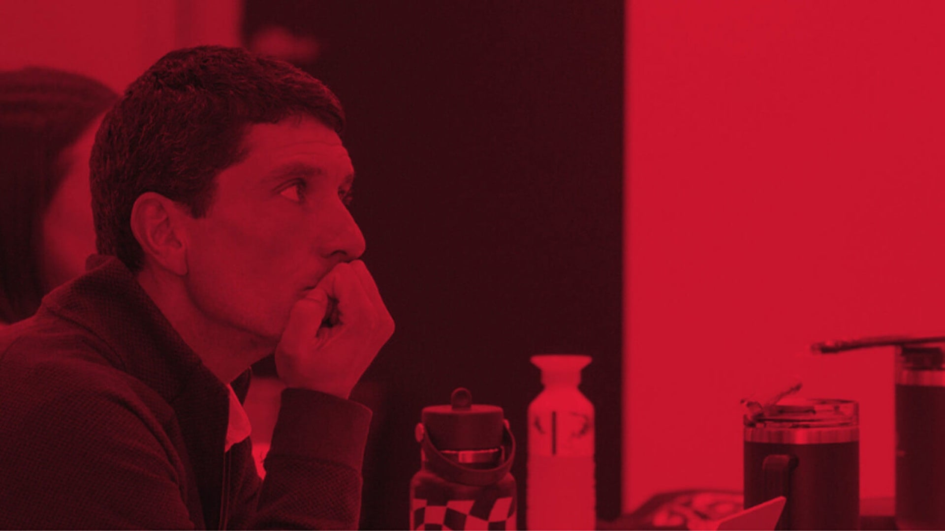 Image includes red overlay of a man intensely looking forward to a speaker out of frame