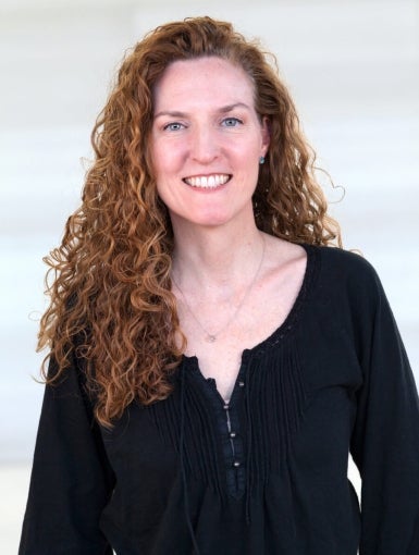 Eva Dixon's headshot features a woman wearing a black shirt with curly red hair